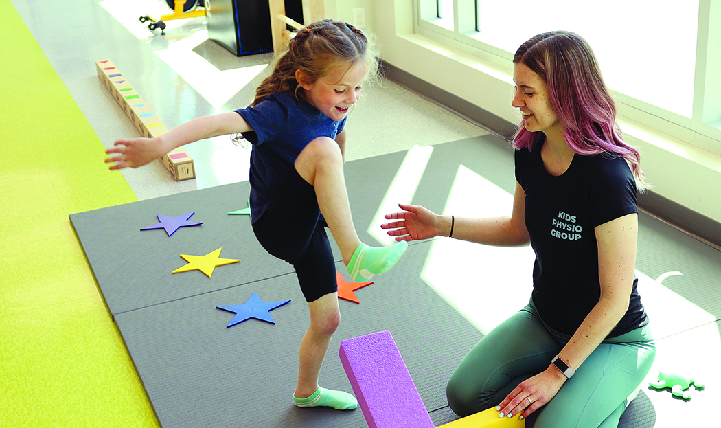 A physiotherapist works with a young child in a colourful environment.