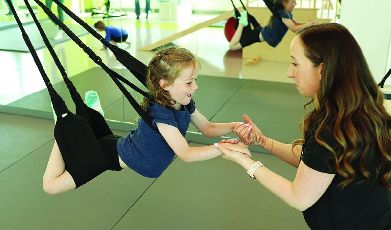 A physiotherapist works with a child using a swing in a gym-like environment.