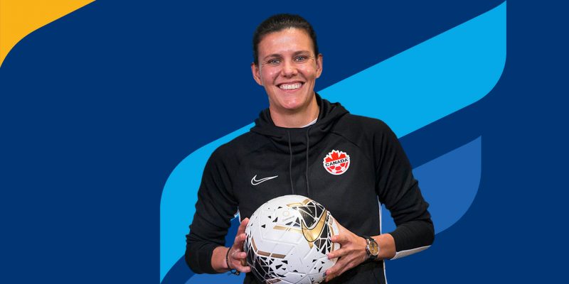 Christine Sinclair holding a soccer ball in front of University of Manitoba branding colours