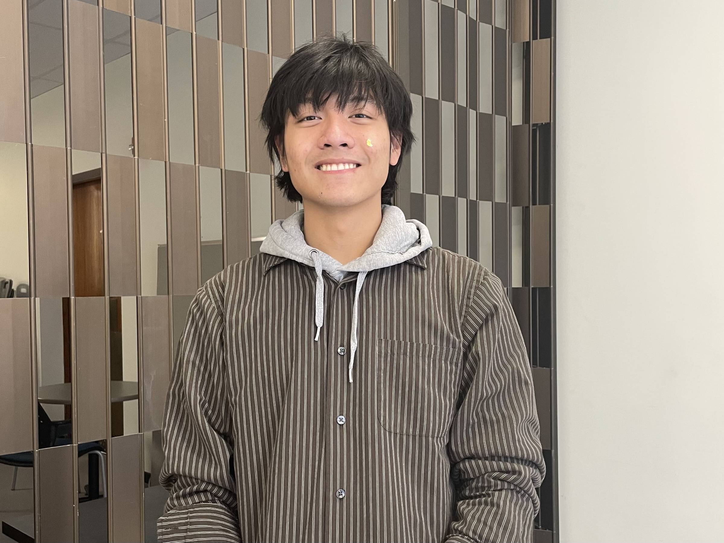 Student in brown hoodie standing in front of a checkered wall.