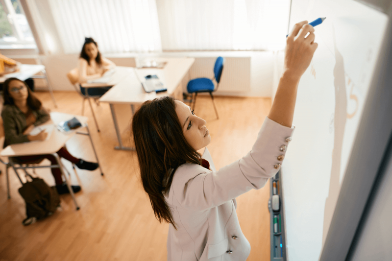 Instructor in classroom writing on a whiteboard