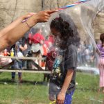 A volunteer creating a big soap and water bubble around a little kid.