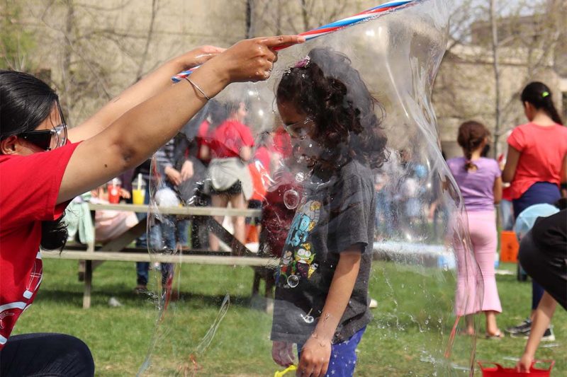 A volunteer creating a big soap and water bubble around a little kid.