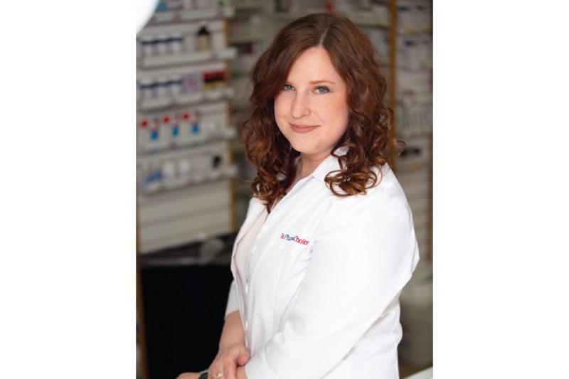 Portrait of Alia Marcinkow in a pharmacy. She is wearing a white pharmacist's coat.