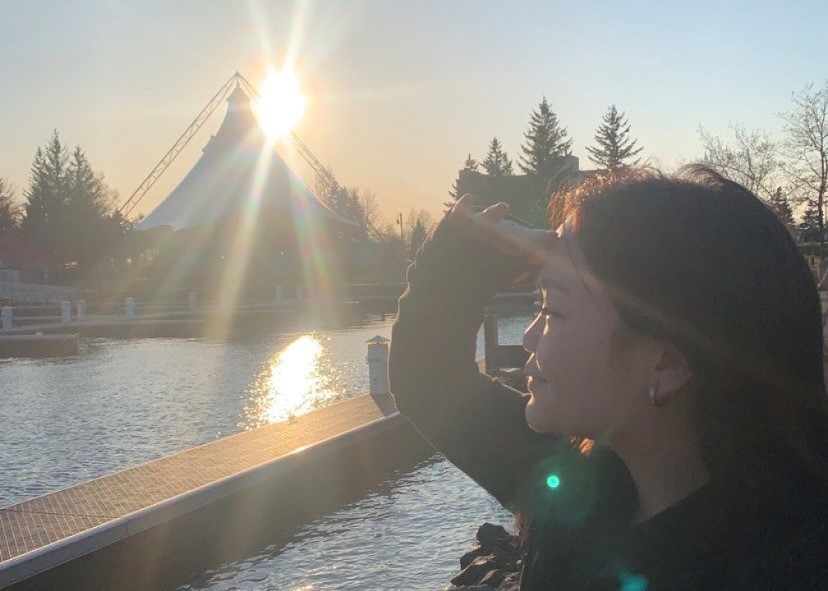 A person looking out over a body of water with a sunset behind a large tent in the background.
