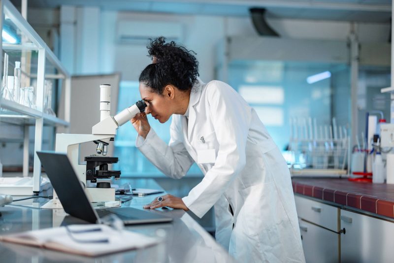 A researcher looks into a microscope in a biomedical lab.