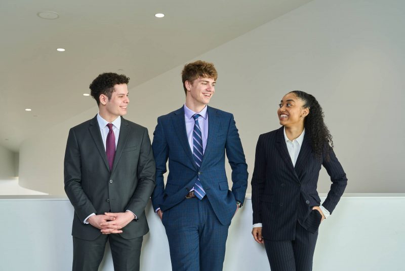 Three students stand looking at each other and grinning.