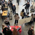 Looking down at a crowd of people looking at project displays on tables and on posters