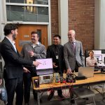 a group of students in conversation by an electrical and computer engineering project displayed on a table