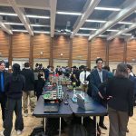 A crowd of students standing in front of table displays of their projects