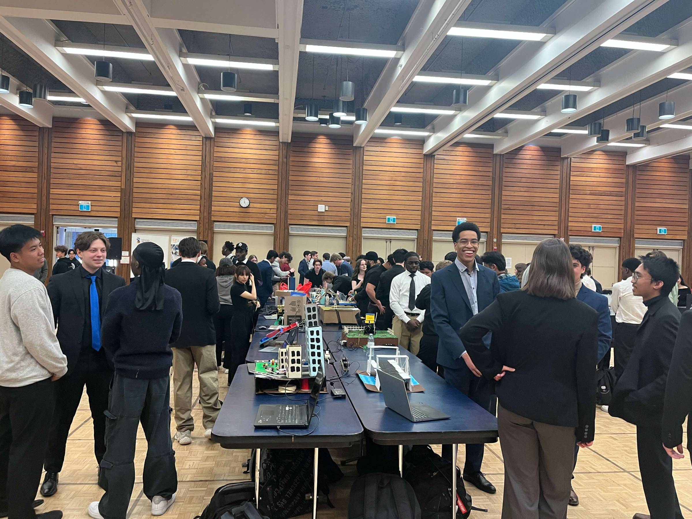 A crowd of students standing in front of table displays of their projects