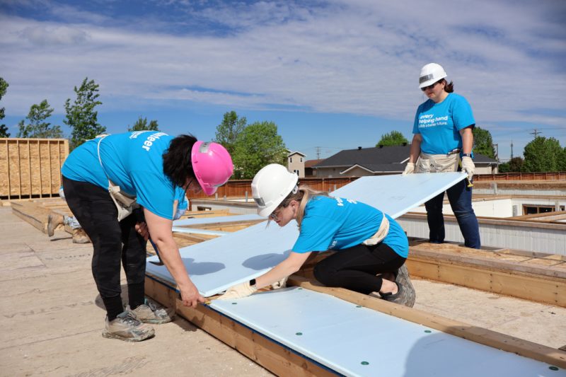 Three people wearing hardhats install construction material. 