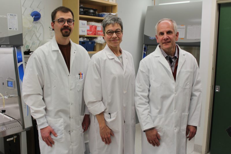 The group poses for a photo in a lab. They are wearing lab coats. 