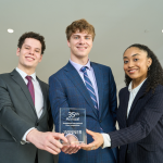 Three students hold up a first-place trophy with pride.