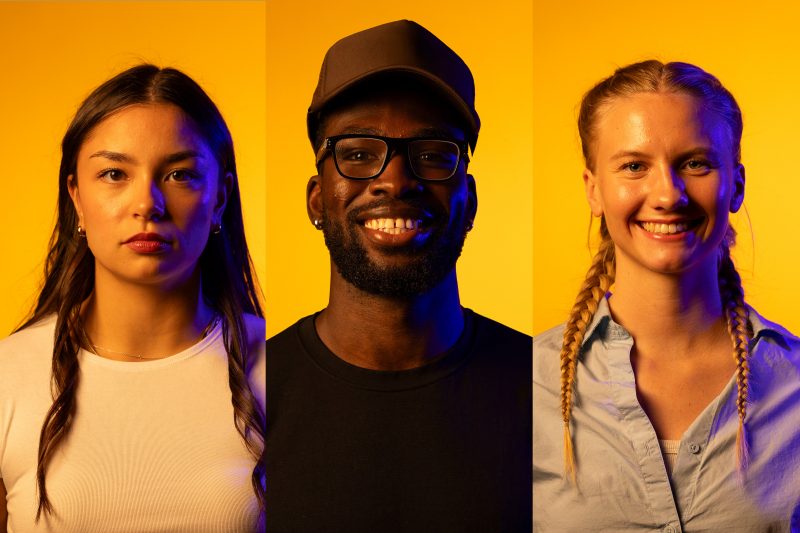 Andie Almonte, Tito Obasoto and Indi Halldorson Haines standing against a gold back drop with blue light mimicing the new Bisons logo