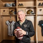 Brian Dobie holding football in front of Bisons Football locker room stalls