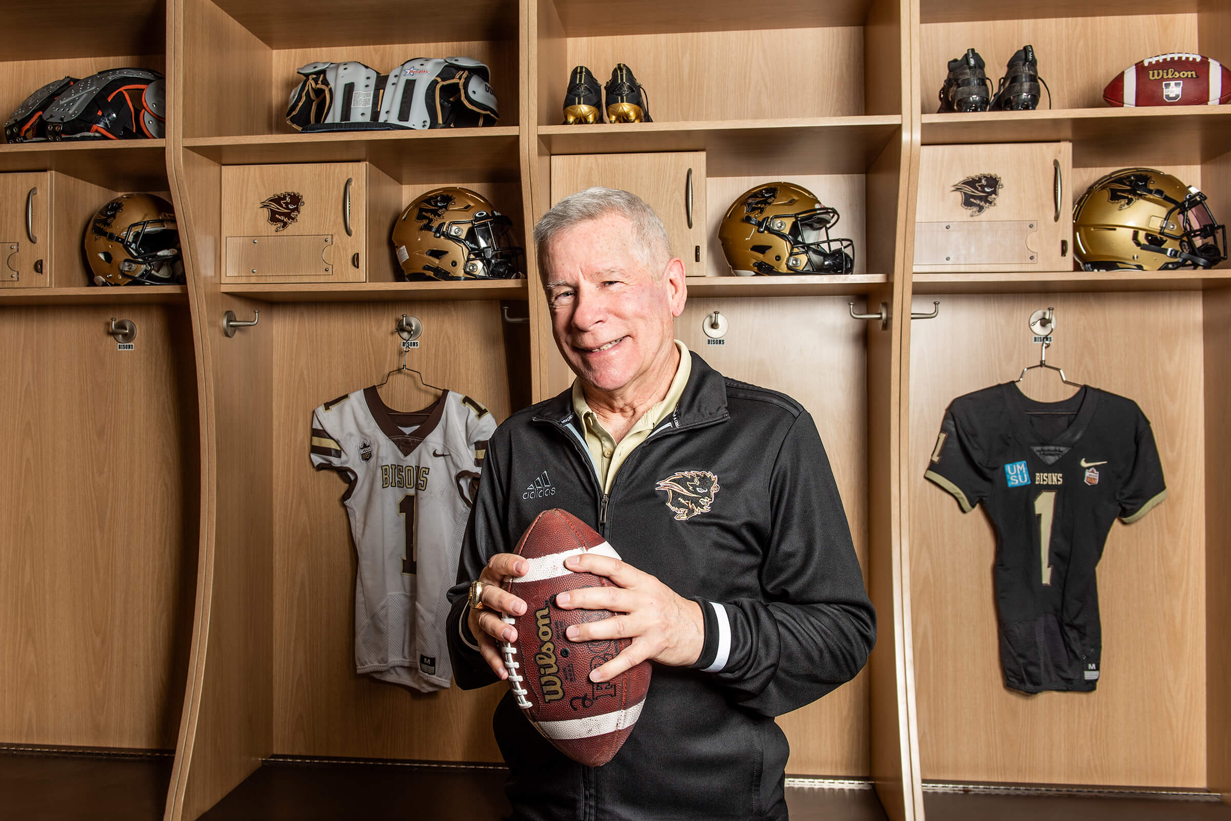 Brian Dobie holding football in front of Bisons Football locker room stalls