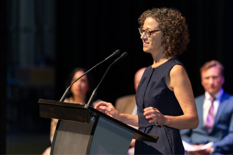 Dr. Marissa Becker speaks into two microphones at a lectern. 