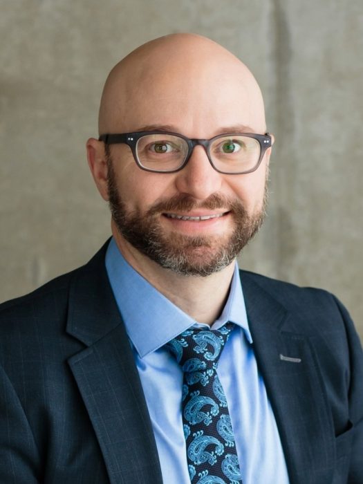 headshot against a gray wall background.