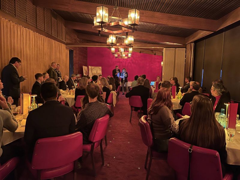 Two people speaking to a crowd of people sitting in a restaurant environment