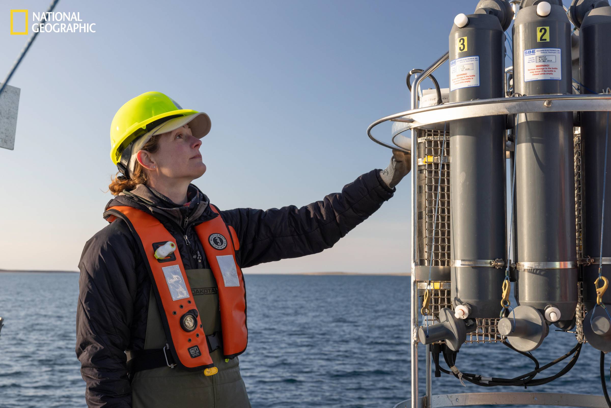 A person is reaching to check on metal bottles that collect ocean water.