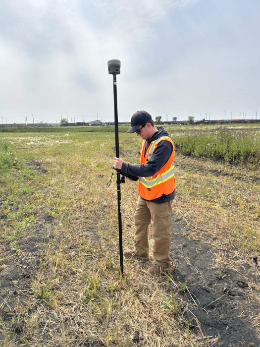 A person in a field wearing a safety vest and holding survey equipment
