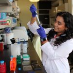Tamarah Singh works with a pipette in a lab. She is wearing gloves and a lab coat.