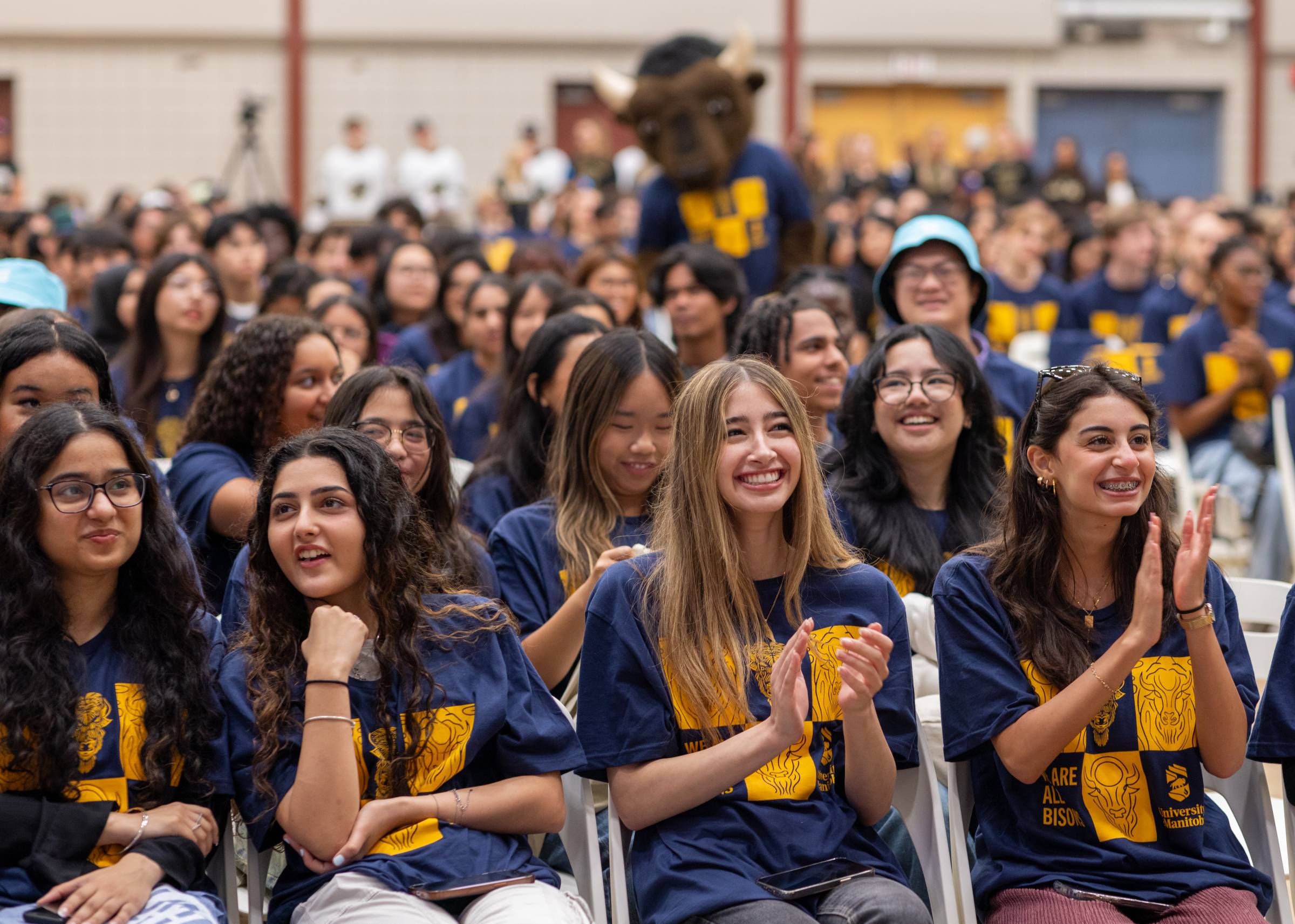 New students in the stands at the welcome day innvcation and pep rally. Students wear their new UM T-Shirt and cheer as Billy the Bison does the same in the background.