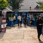 Students visiting outdoor information booths with tents, banners, and tables set up for campus services and clubs.
