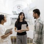 Three students standing in a hallway talking.
