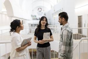 Three students standing in a hallway talking.