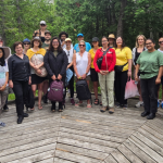 A group of Summer Institute participants posing for a photo on a wooden platform in the forest.