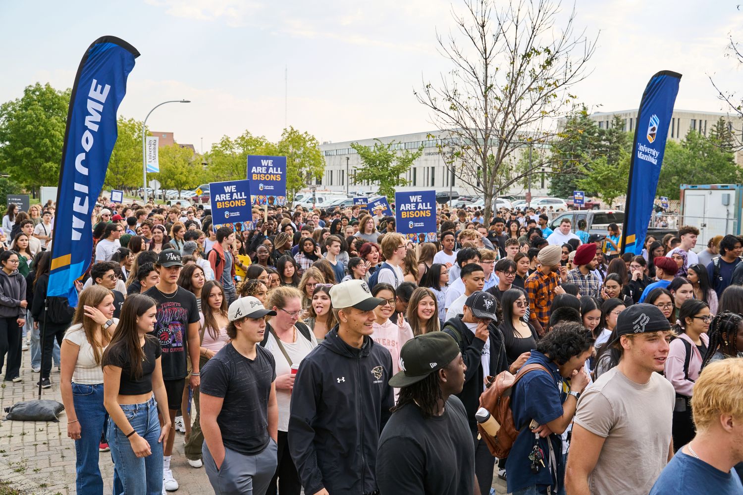 A large group of new UM students gather outside signs stating "We are all Bisons"