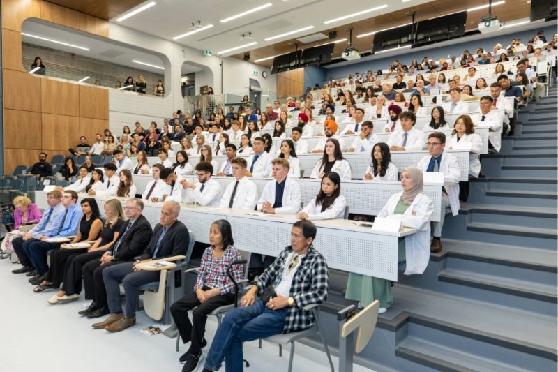 Pharmacy students seated at the centre of an amphitheatre-style classroom, with other event attendees dispersed throughout the theatre.