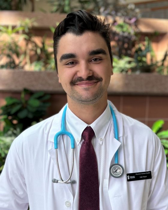 Portrait of Kale Mayor. He is wearing a white coat and a stethoscope around his neck.