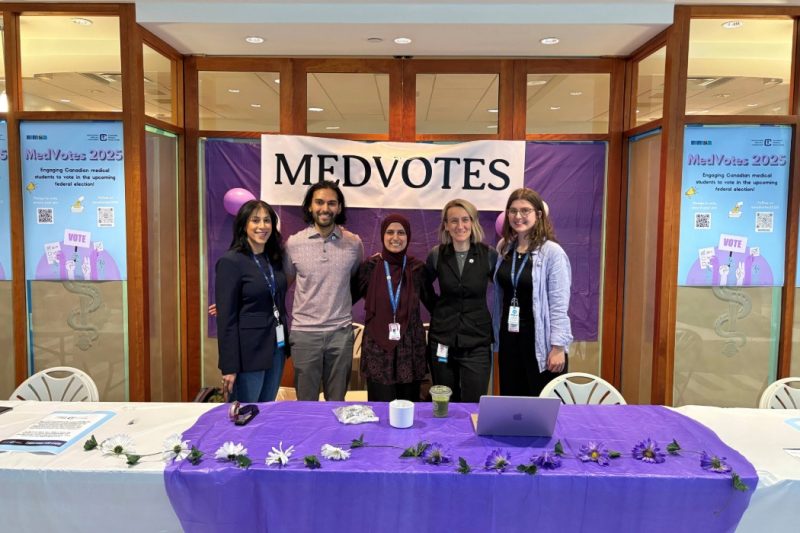 Five people smiling at the camera, standing behind a table at the MedVotes booth.