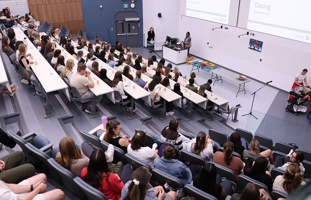 A large class of students at an Indigenous ceremony in a lecture hall.