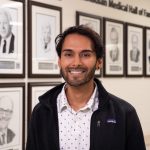 Akhil Ramdoyal smiling in front of the Canadian Medical Hall of Fame Laureates wall at the UM Bannatyne campus.