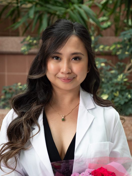 Yves Earielle Pua Robleza, College of Pharmacy student in white coat smiling at the camera while holding a bouquet of flowers.