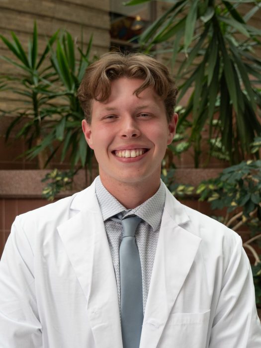 Leif Robak, College of Pharmacy student in white coat smiling at the camera.
