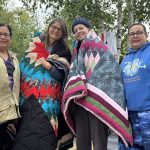 Lisa Mendez and Maura Macaulay wear star blankets and pose alongside Esther Cook and Margaret McGregor at Misipawistik Cree Nation.