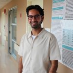 Portrait of Jai Sareen standing next to a research poster in a hospital hallway.