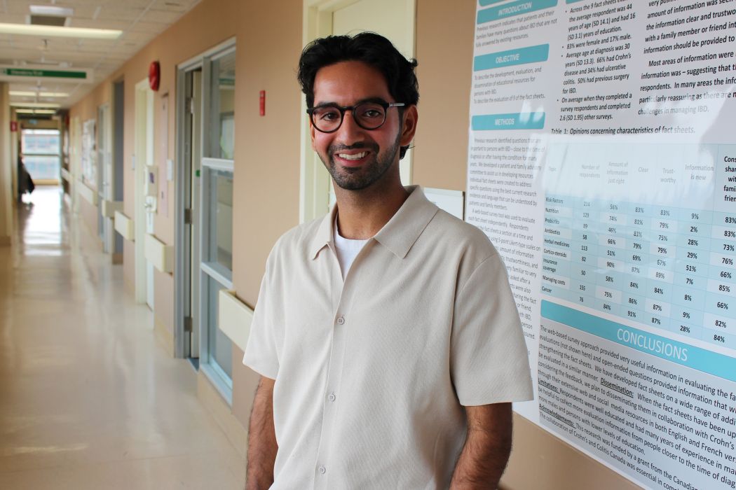 Portrait of Jai Sareen standing next to a research poster in a hospital hallway.