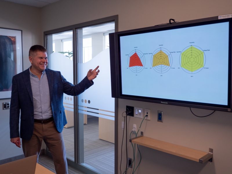Barret Monchka presents while pointing at a screen displaying a presentation slide.