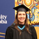 Jessica Smart stands in front of a University of Manitoba banner wearing a convocation cap and gown.