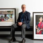 James Blanchard, Executive Director of UM's Global Institute of Public Health, sits on a bench, with a framed photos on either side