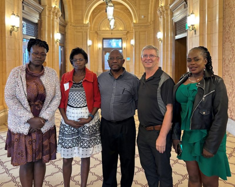 Five people pose for a photo in a fancy, old hotel hallway.