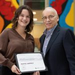 Katie Leppky and Lyle Silverman smile at the camera while Leppky holds an award certificate.