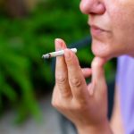A woman holds a lit cigarette between her fingers.
