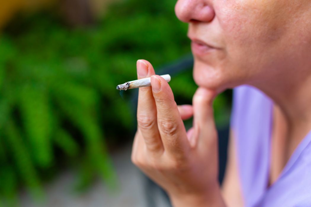 A woman holds a lit cigarette between her fingers.